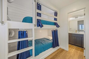 A bunk bed room with a fan, a bathroom with a mirror, and a wooden floor. - Brand New Semi-Oceanfront Waves Home with Private Pool, Hot Tub and Game Room (Waves)