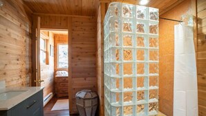 Interior de una cabaña de madera con baño que incluye una ducha con mampara de vidrio y suelo de madera.
