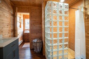 Ein Holzblock-Innenraum mit einem Badezimmer, das eine Duschkabine aus Glas und einen Holzboden zeigt.