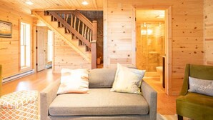 Interior acogedor de una cabaña con sofá, escalera y paredes de madera.