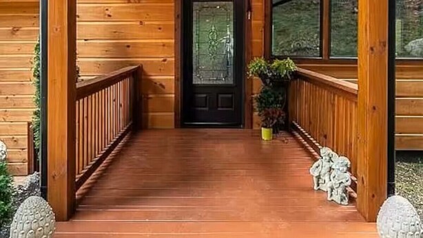 Una cabaña de madera con un porche, una puerta negra y dos lámparas de estilo farol.