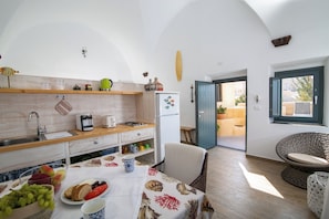 Una cocina moderna con armarios de madera, una mesa de comedor dispuesta con frutas y una cafetera, y vistas al exterior.