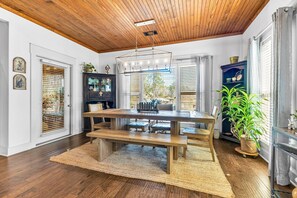 A dining area with a wooden table and benches, a chandelier, and a large potted plant.
