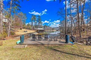 A wooden deck with outdoor seating, a pond, and a gazebo in a wooded area.