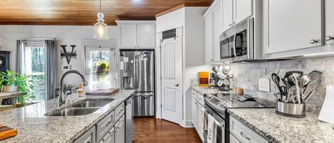 A modern kitchen with granite countertops, stainless steel appliances, and a wooden ceiling.