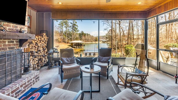 Un espacio al aire libre acogedor con una chimenea, sillas cómodas y vistas a un lago y árboles.