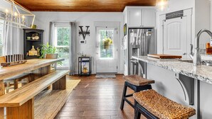 Una cocina moderna con piso de madera, un banco de madera, un estante negro con objetos decorativos y una puerta blanca con ventanal.
