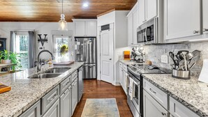 Una cocina moderna con encimeras de granito, electrodomésticos de acero inoxidable y techo de madera.