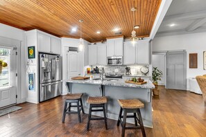A modern kitchen with white cabinets, stainless steel appliances, a marble island, and three woven stools.