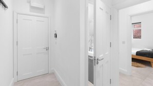 A hallway with a closed door, a white wall, and a window with a brick wall visible through it. - Modern 4 Bedroom Apartment in London with Parking + Garden (London)