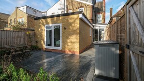 A residential property with a brick exterior, a covered patio, and a small garden area. - Modern 4 Bedroom Apartment in London with Parking + Garden (London)