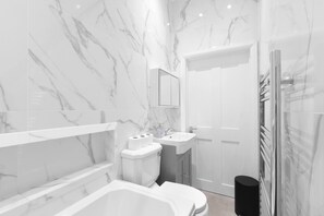 A modern bathroom with a marble backsplash, a toilet, a sink, and a shower area. - Modern 4 Bedroom Apartment in London with Parking + Garden (London)