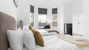 A modern hotel room with two beds, a desk, and a view of the street. - Modern 4 Bedroom Apartment in London with Parking + Garden (London)