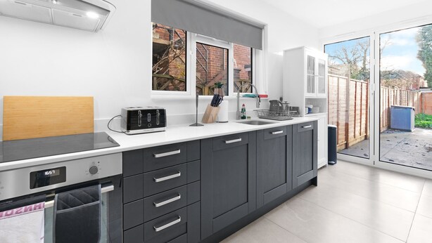 A modern kitchen with a built-in oven, a microwave, and a toaster. There is a window above the sink and a sliding glass door leading to a patio. - Modern 4 Bedroom Apartment in London with Parking + Garden (London)