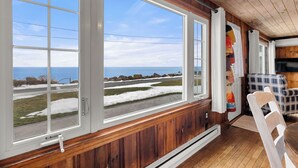 Ein Zimmer mit großen Fenstern, das auf eine verschneite Landschaft und das Meer blickt.