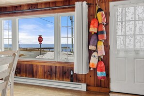Un intérieur en bois offrant une vue sur l’océan grâce à de grandes fenêtres, un panneau de signalisation à l’extérieur et des objets décoratifs colorés accrochés au mur.