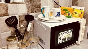 A kitchen counter with a microwave, a coffee maker, a box of Lipton tea, and some kitchen utensils.