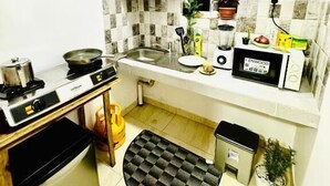 A compact kitchen with a gas stove, a microwave, and a sink. There is a window above the sink, and a small potted plant on the windowsill.