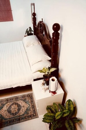 A neatly made bed with white linens, a wooden headboard, and a bedside table with a plant and a decorative item. - House of Sincerity  (Maharagama)