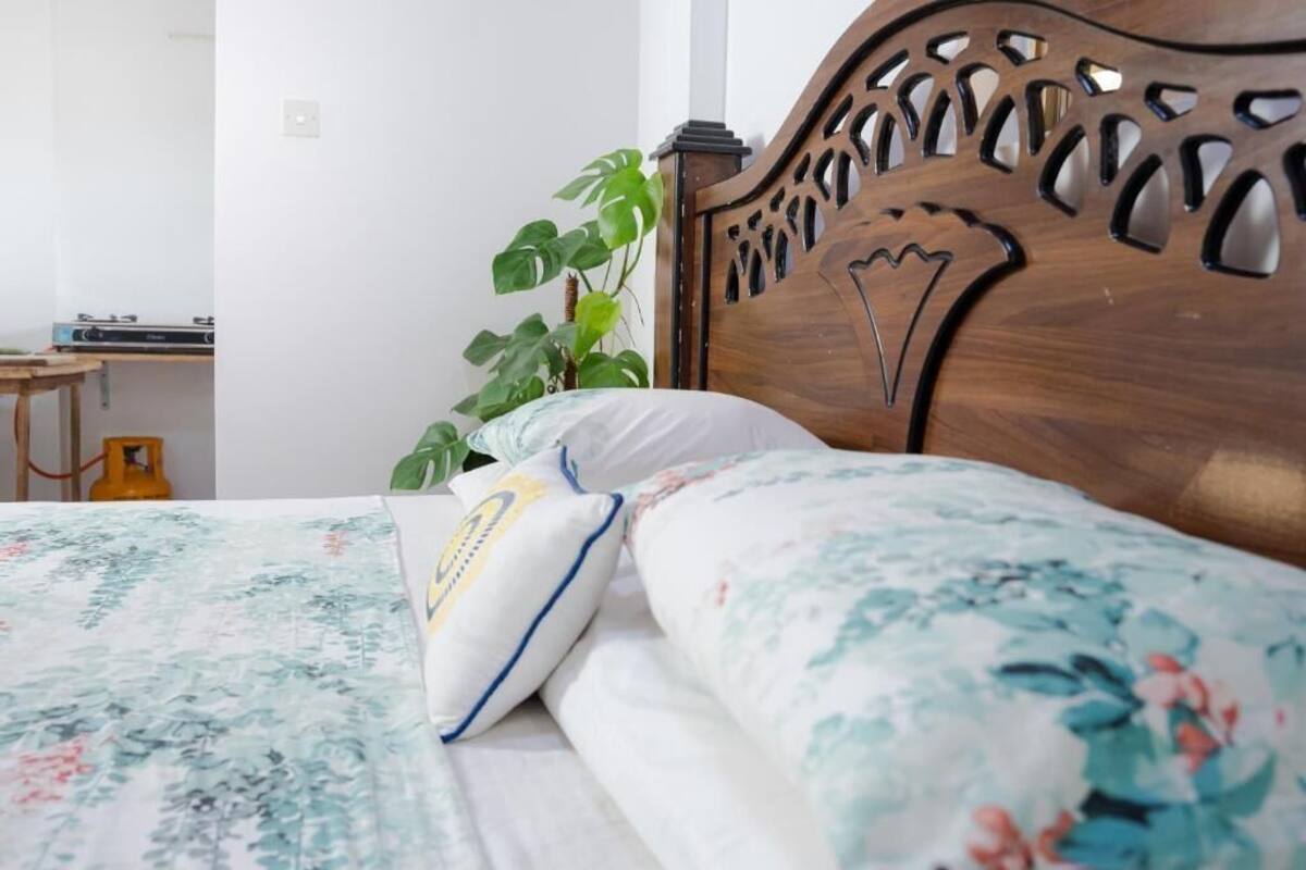 A bed with a floral bedspread and two pillows, a wooden headboard with intricate cut-out designs, and a green plant beside the bed.