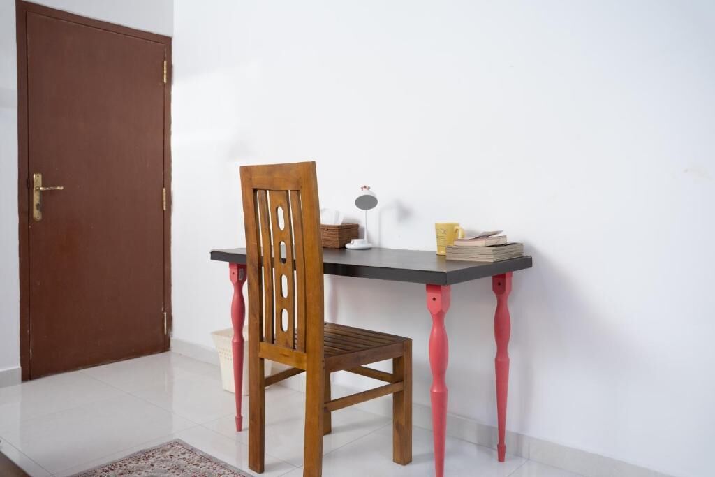 A small room with a wooden chair, a desk with a lamp, and a door.