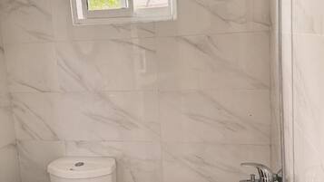 A bathroom with marble tiles, a toilet, and a shower.
