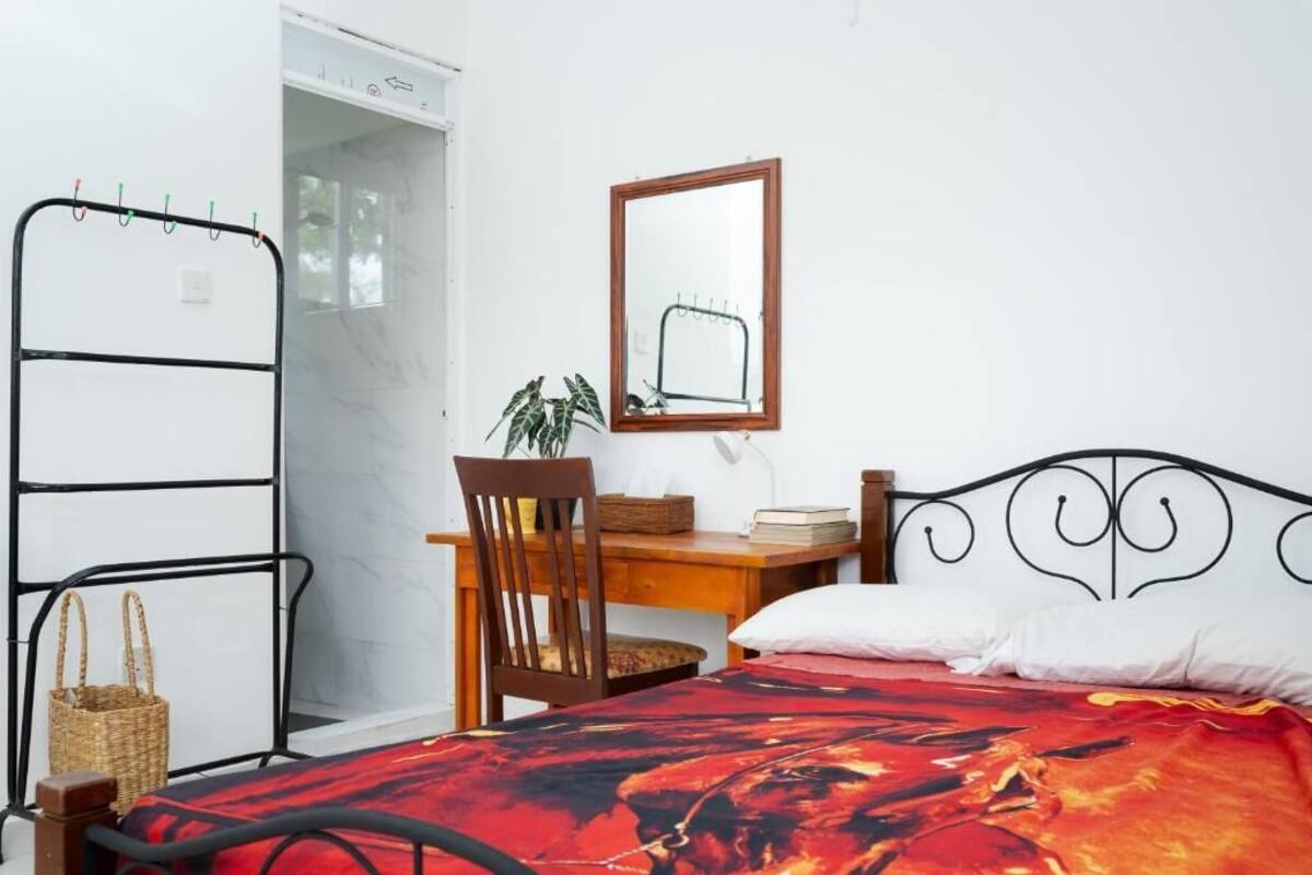 A bedroom with a bed, a desk, a chair, a mirror, and a wardrobe.