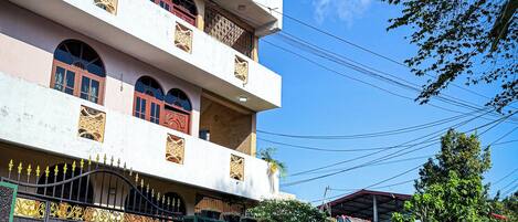 A multi-story building with balconies, a gated entrance, and a street in front.