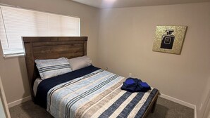 Ein Schlafzimmer mit Bett, Deckenventilator, Fenster mit Jalousien und einem Wandbild.