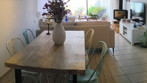 A dining area with a wooden table, chairs, a vase with flowers, a sofa, a television, and a view of the outdoors. - House with pool 1 km from Sitges beach (Sant Pere de Ribes)