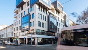 Ein mehrstöckiges Gebäude mit einem Starbucks Coffee im Erdgeschoss, ein vorbeifahrender Straßenbahn und eine Fußgängerampel.