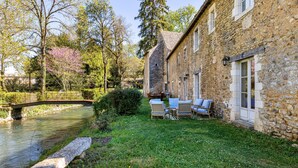 Ein Steingebäude mit Garten, einer kleinen Brücke und Außenplätzen am Fluss.