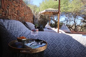 A stone wall, patterned cushions, a tray with sunglasses and a book, and a wooden table. - Last Word Makanyane (Thabazimbi)
