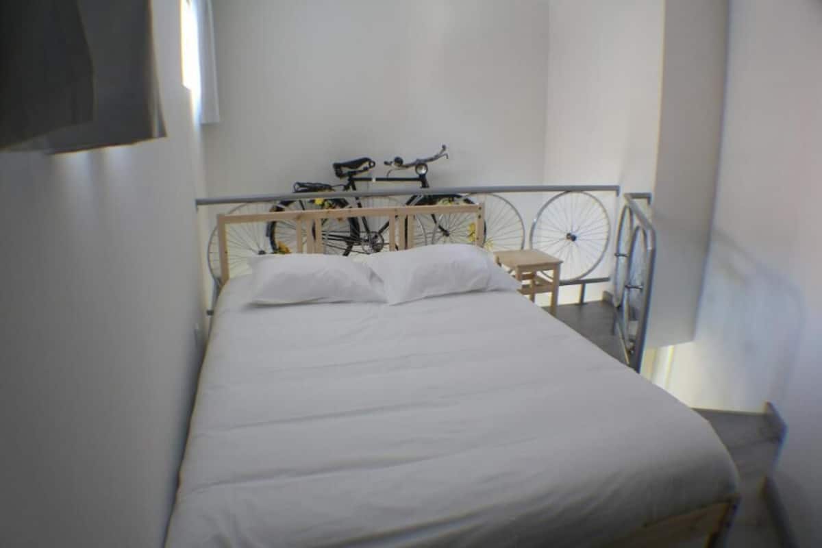A single bed with white bedding in a room with a bicycle rack against the wall.