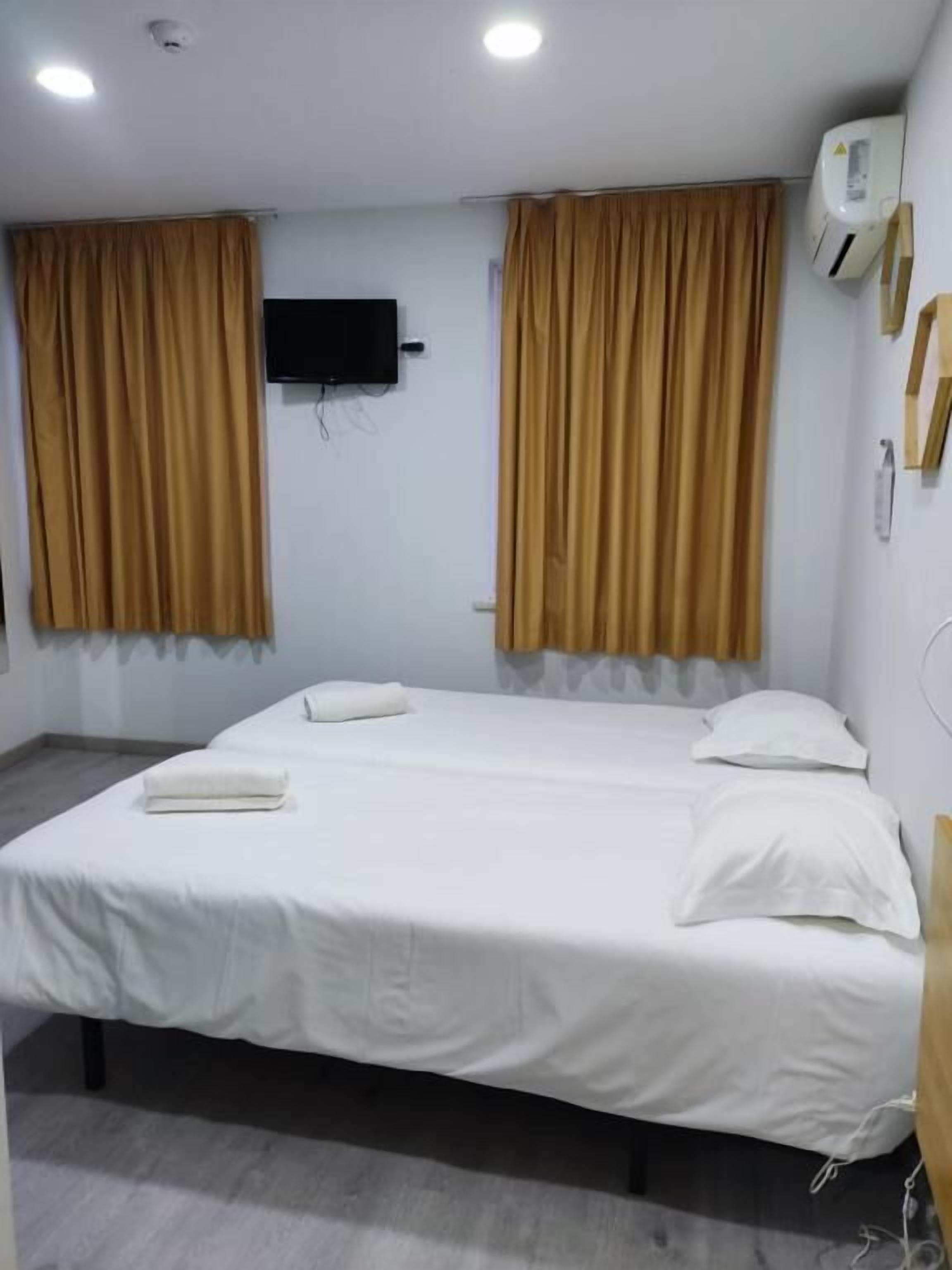Une chambre d’hôtel avec deux lits, un téléviseur à écran plat, un système de climatisation et des rideaux.