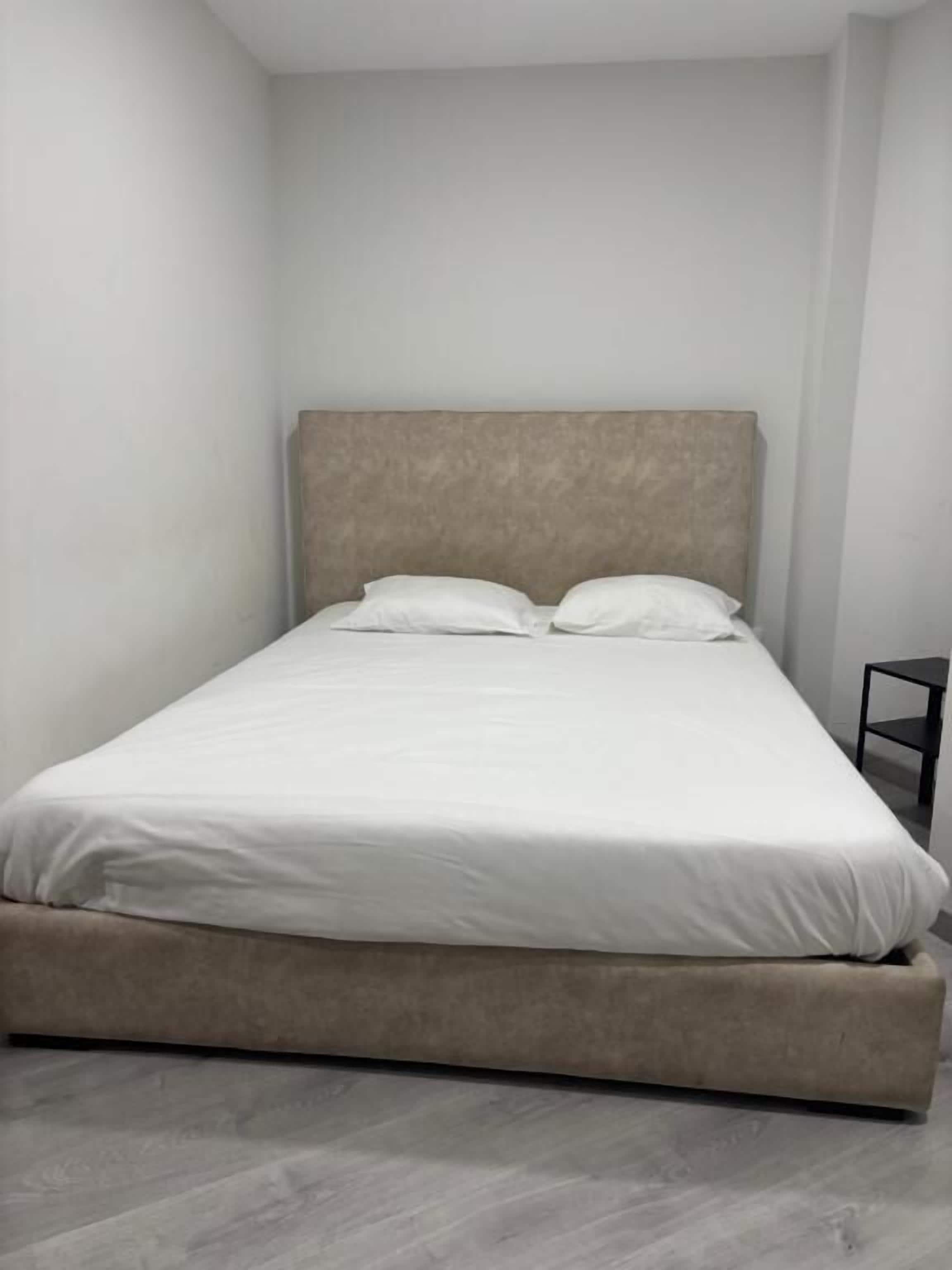 A single bed with a headboard, white bedding, and a small black nightstand beside it.