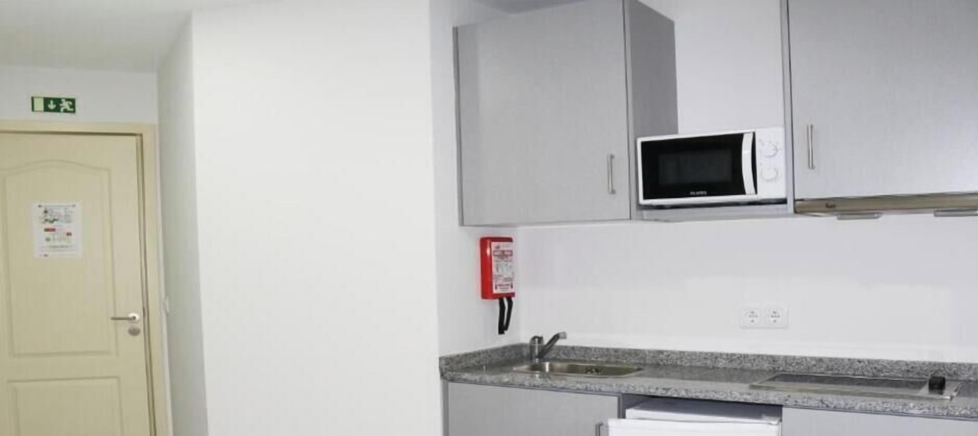 A kitchen with a microwave, a sink, cabinets, and a door with an exit sign.