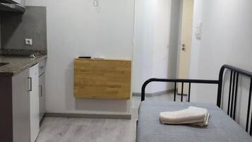 A compact room with a bed, a small kitchenette, a wooden cabinet, a television, and a door leading to another room.