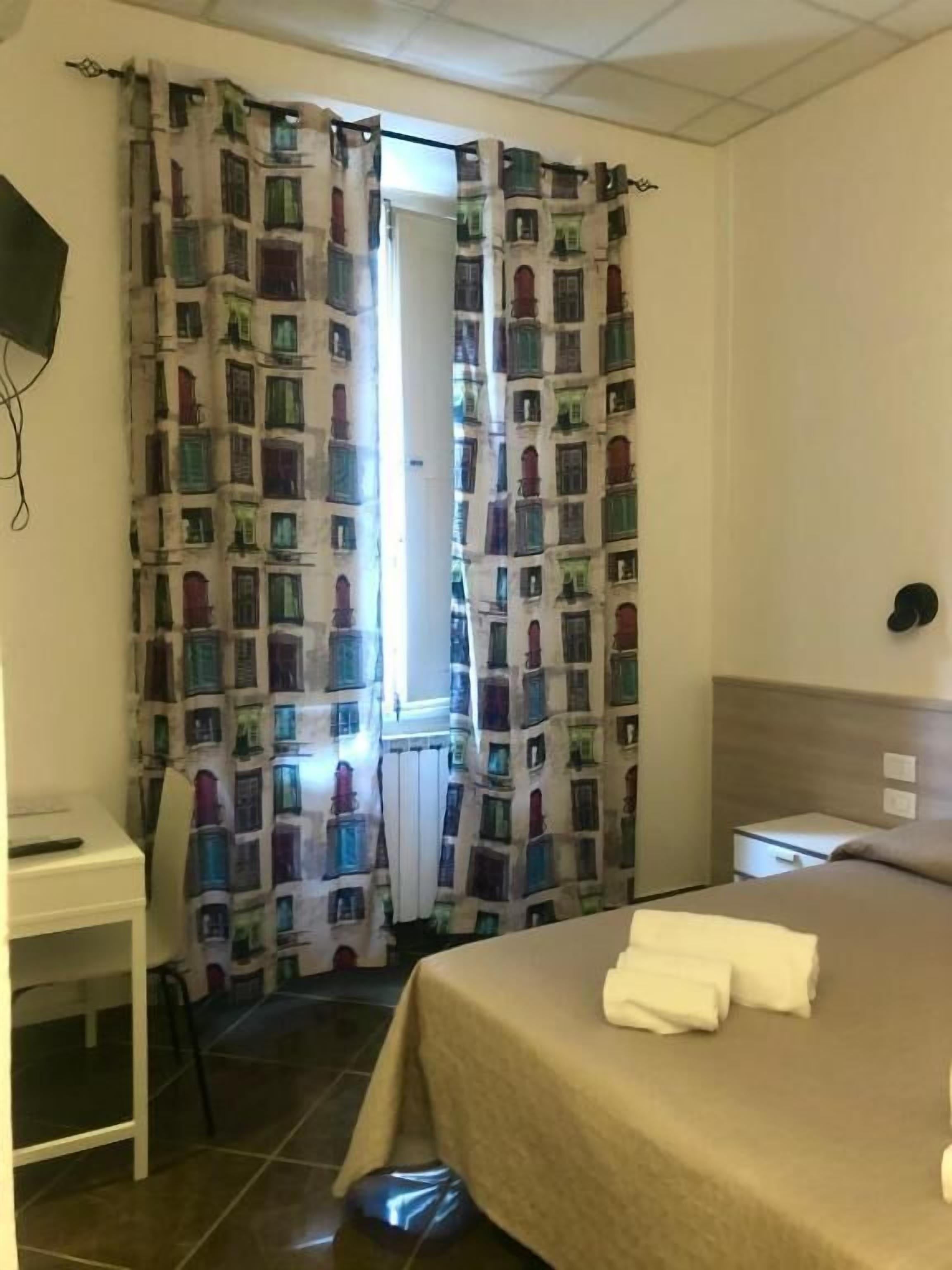 A hotel room with a bed, a bedside table, a nightstand, a curtain with a building pattern, and a wall-mounted TV.