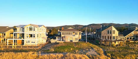 A coastal residential area with multi-story houses, a grassy foreground, and a mountainous backdrop.