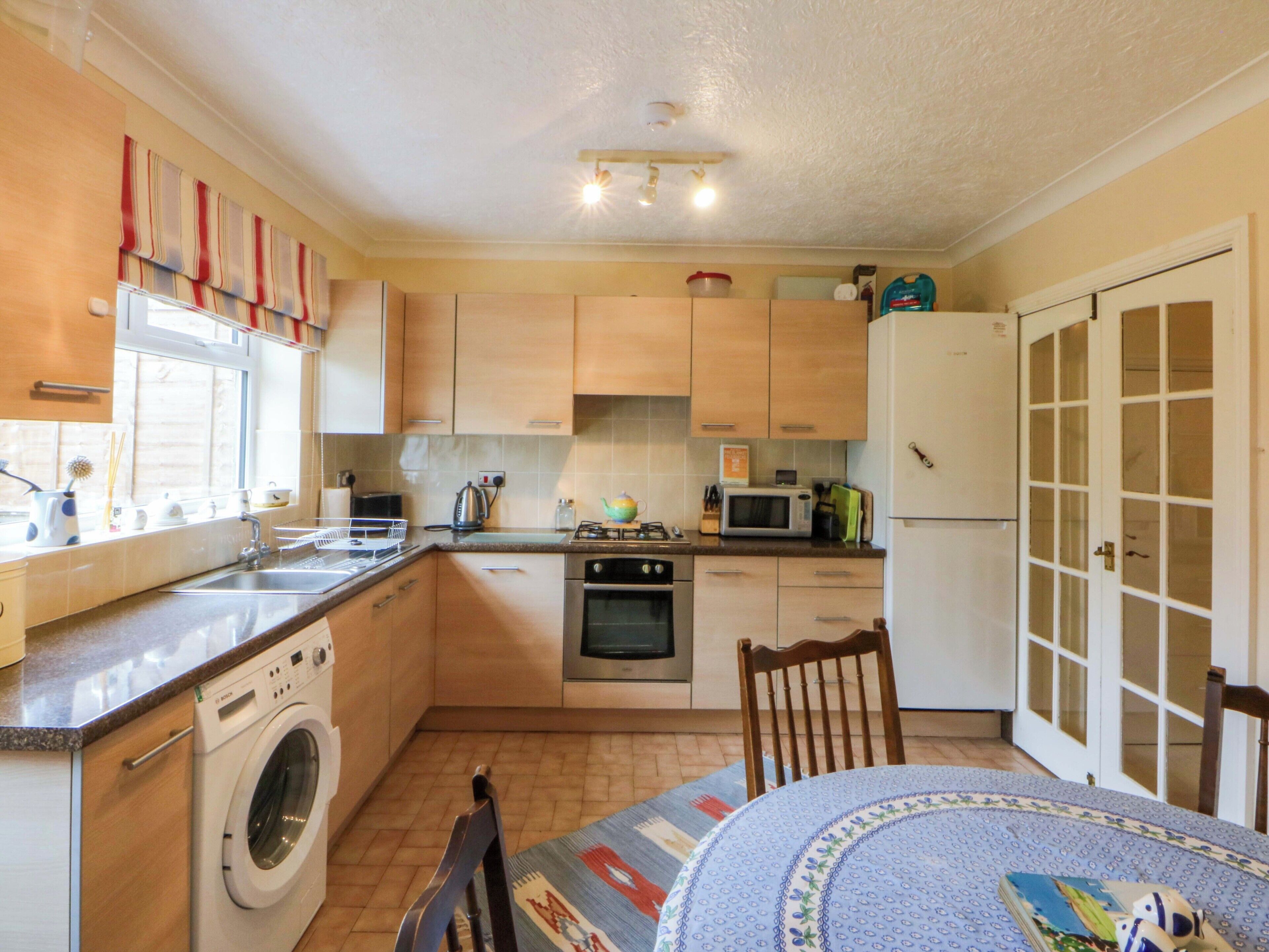 A compact kitchen with a washing machine, oven, microwave, and a dining area with a table and chairs.
