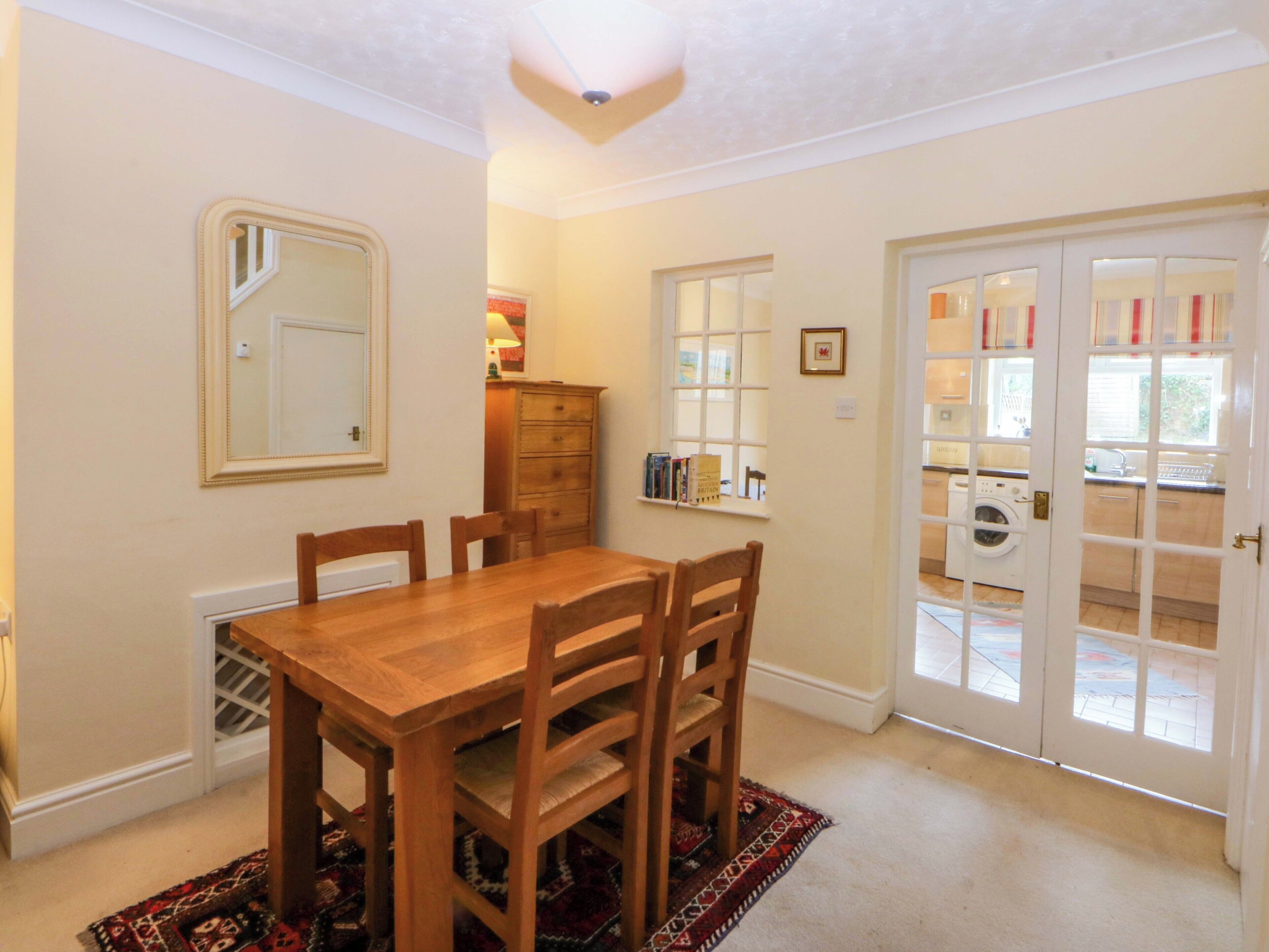 A dining area with a wooden table and chairs, a mirror, a dresser, and a view through a glass door to a laundry area.