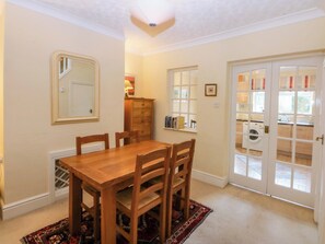 A dining area with a wooden table and chairs, a mirror, a dresser, and a view through a glass door to a laundry area. - 15 Rose Hill (Beaumaris)