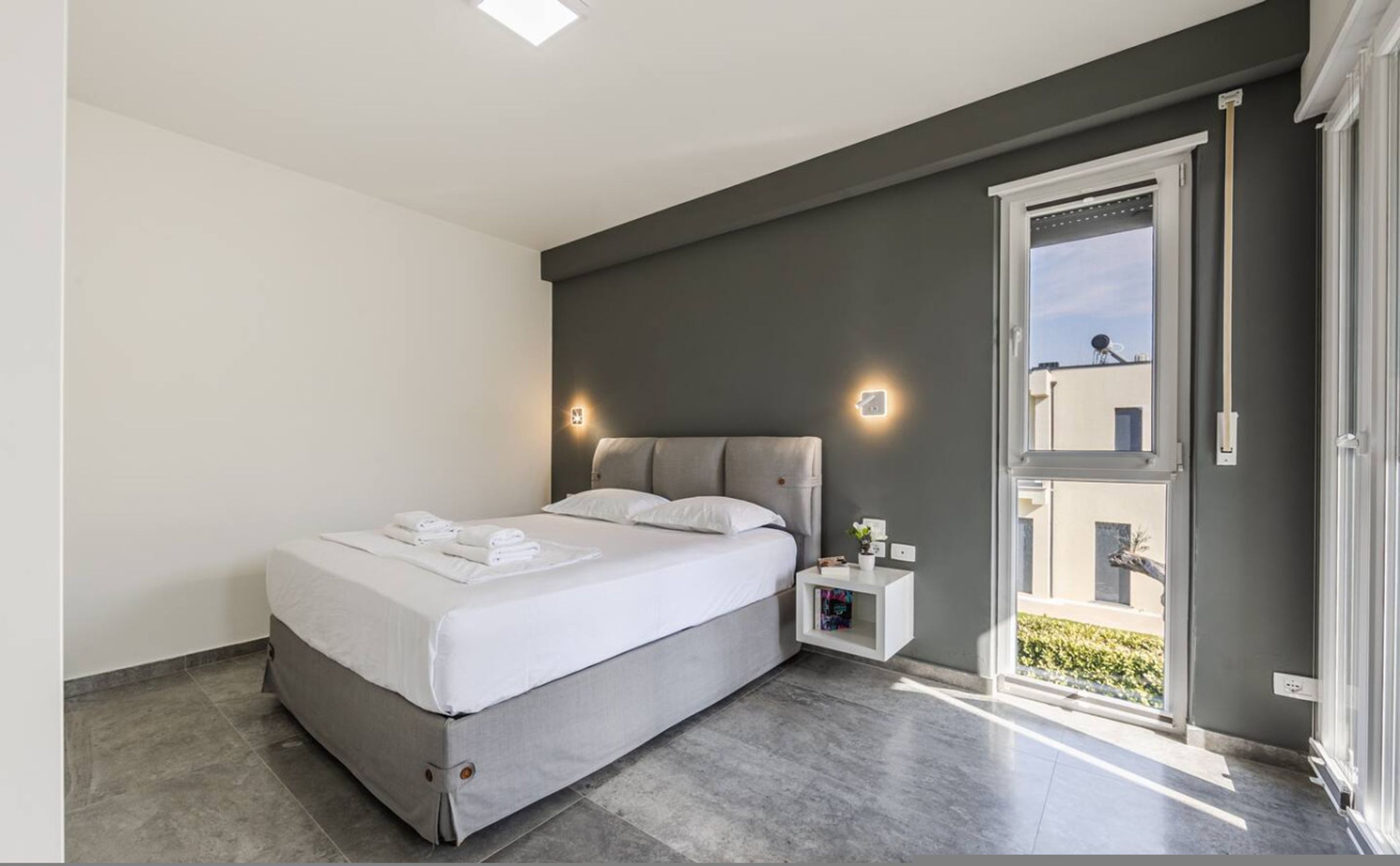 A modern bedroom with a bed, bedside tables, and a view of the outside.