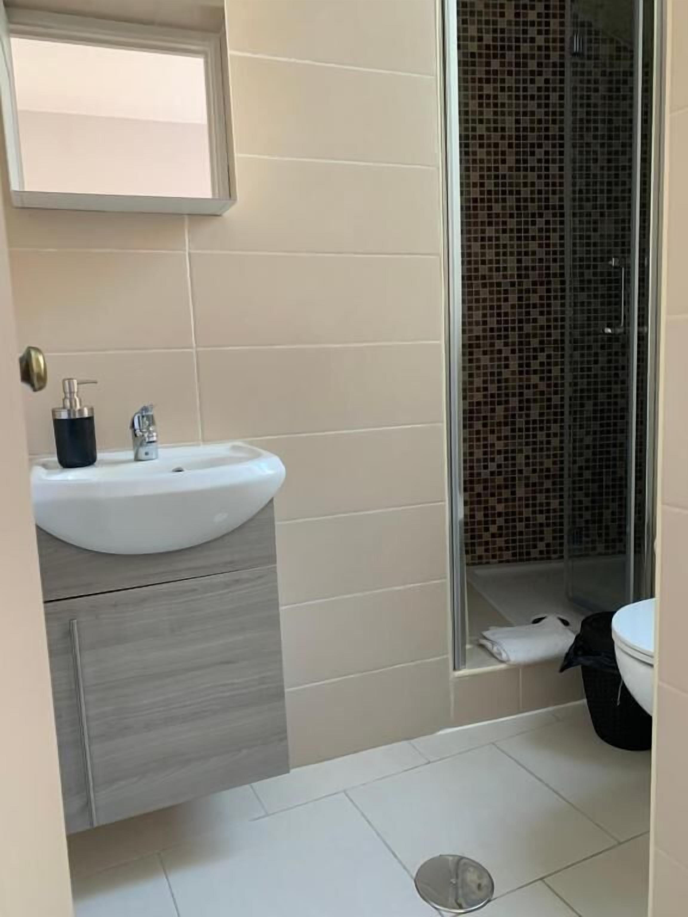 Een badkamer met wastafel, spiegel en douche.