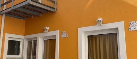 A building with a yellow exterior, a balcony with a wooden railing, and two doors with curtains.
