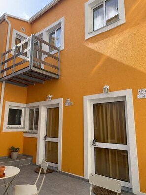 A building with a yellow exterior, a balcony with a wooden railing, and two doors with curtains. - Vila dos Avós (Figueira da Foz)