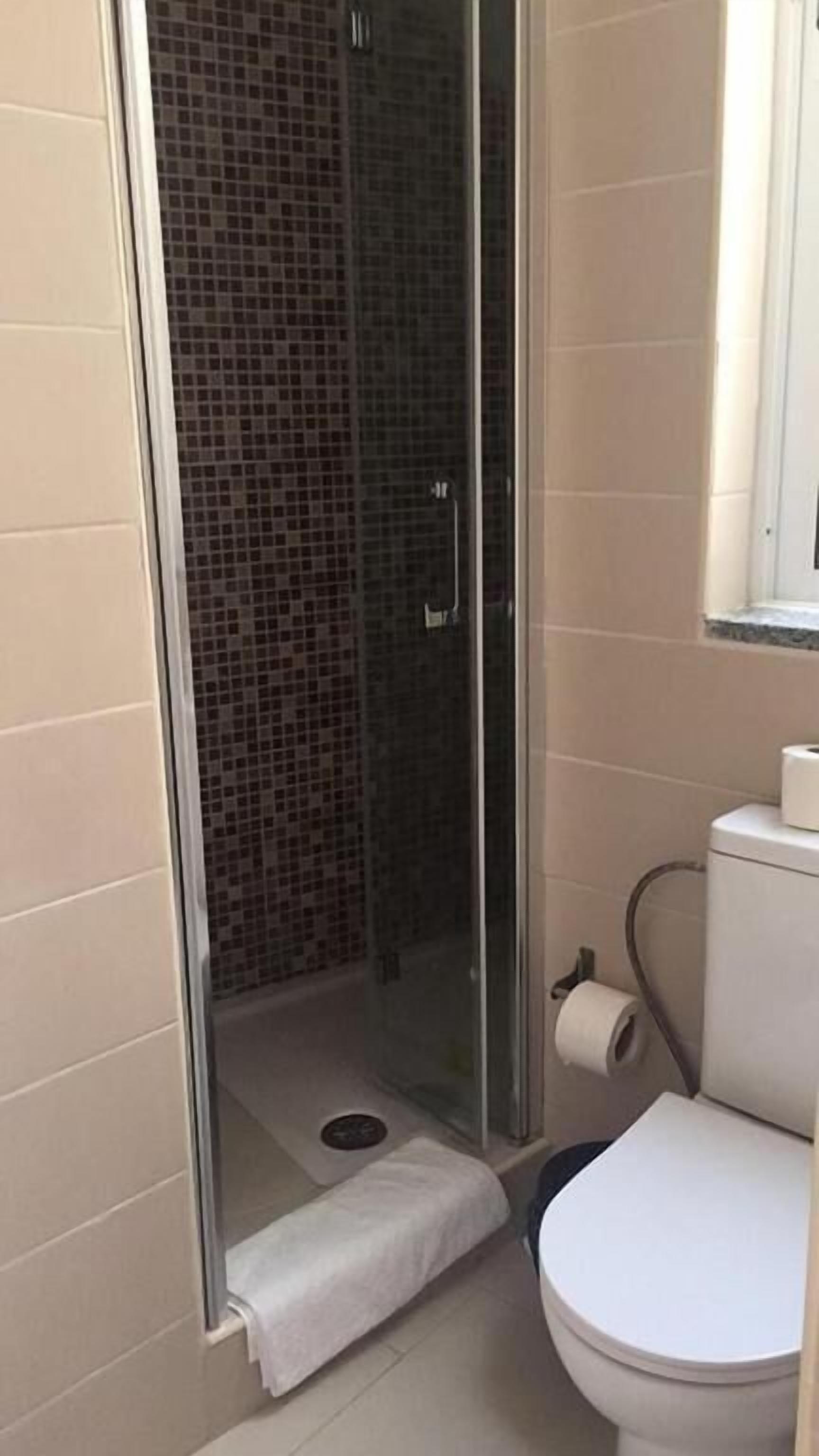 A bathroom with a glass-enclosed shower, a toilet, and a roll of toilet paper on the wall.