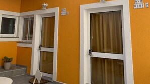 A building with orange walls, white-framed windows, a metal staircase, and a sign indicating room numbers.