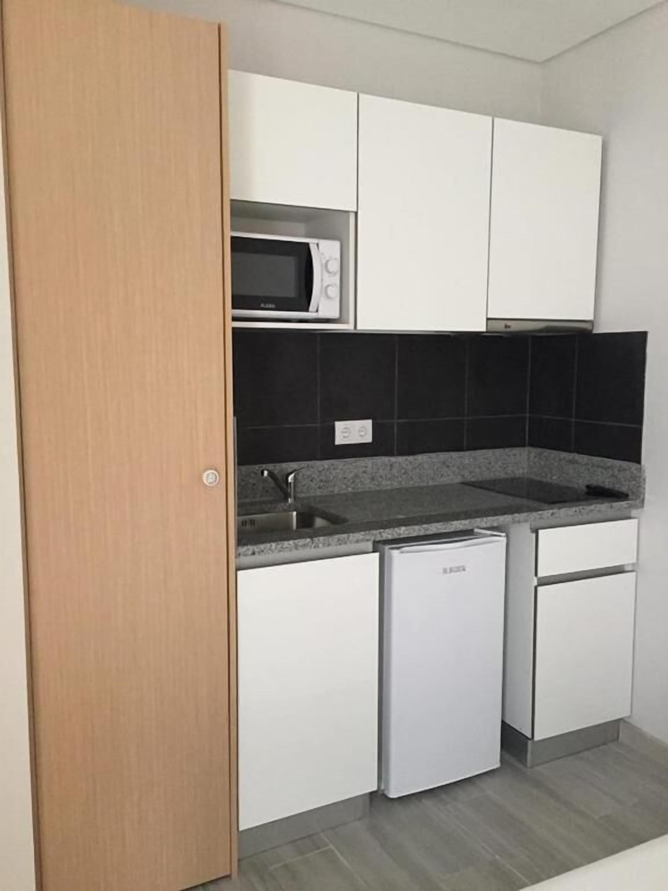 Uma cozinha compacta com armários brancos, micro-ondas, lava-louças e bancada de granito.